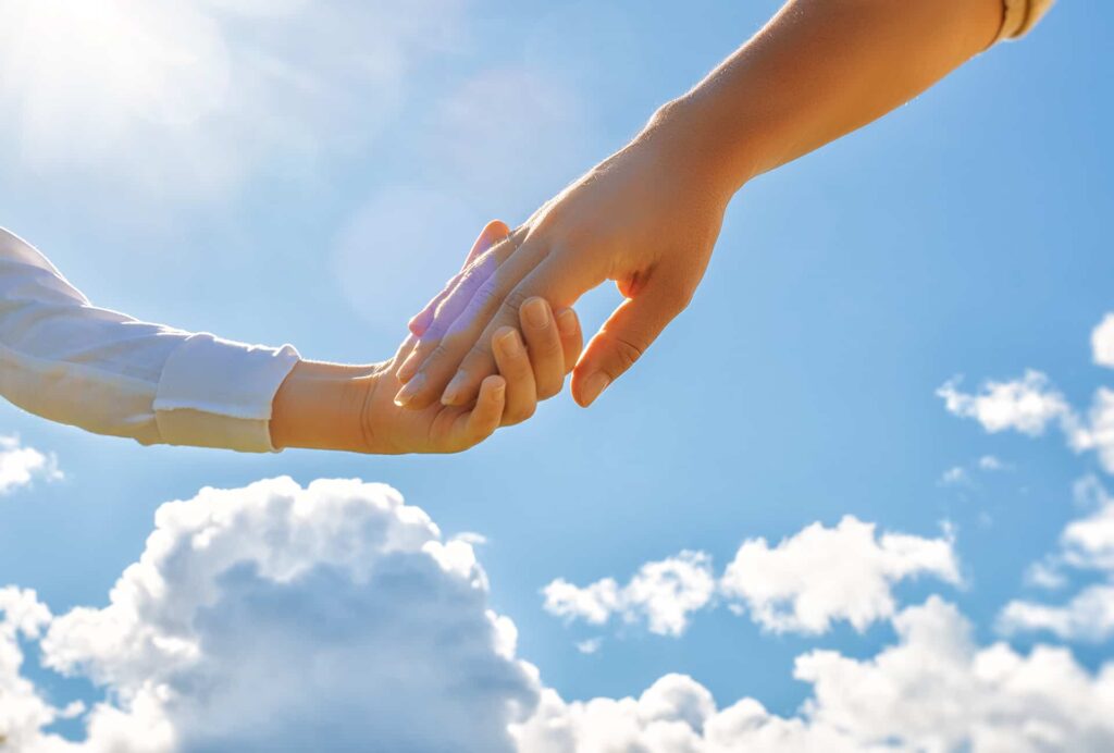 Two hands gently holding each other against a bright blue sky with white clouds, symbolizing the trust and collaboration involved in being a corporate executor.